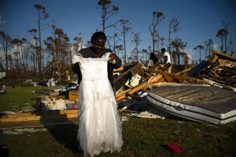 En esta imagen, tomada el 8 de septiembre de 2019, Synobia Reckley muestra el vestido que llevó su sobrina a su boda, mientras busca entre los escombros de su casa, que quedó destrozada por el paso del huracán Dorian