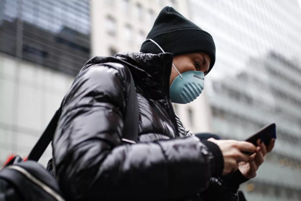 Una persona usa su teléfono celular, y también su máscara, para protegerse del coronavirus